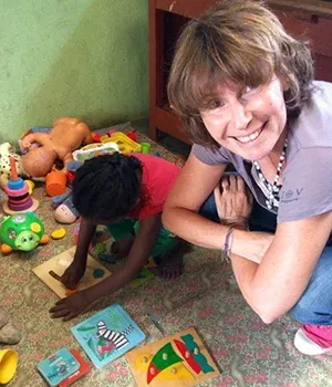 Une femme souriante joue avec un enfant sur un tapis coloré entourés de jouets à Madagascar