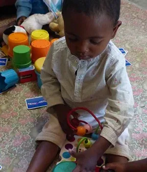 Enfant assis sur tapis coloré jouant avec jouets éducatifs et anneaux empilables