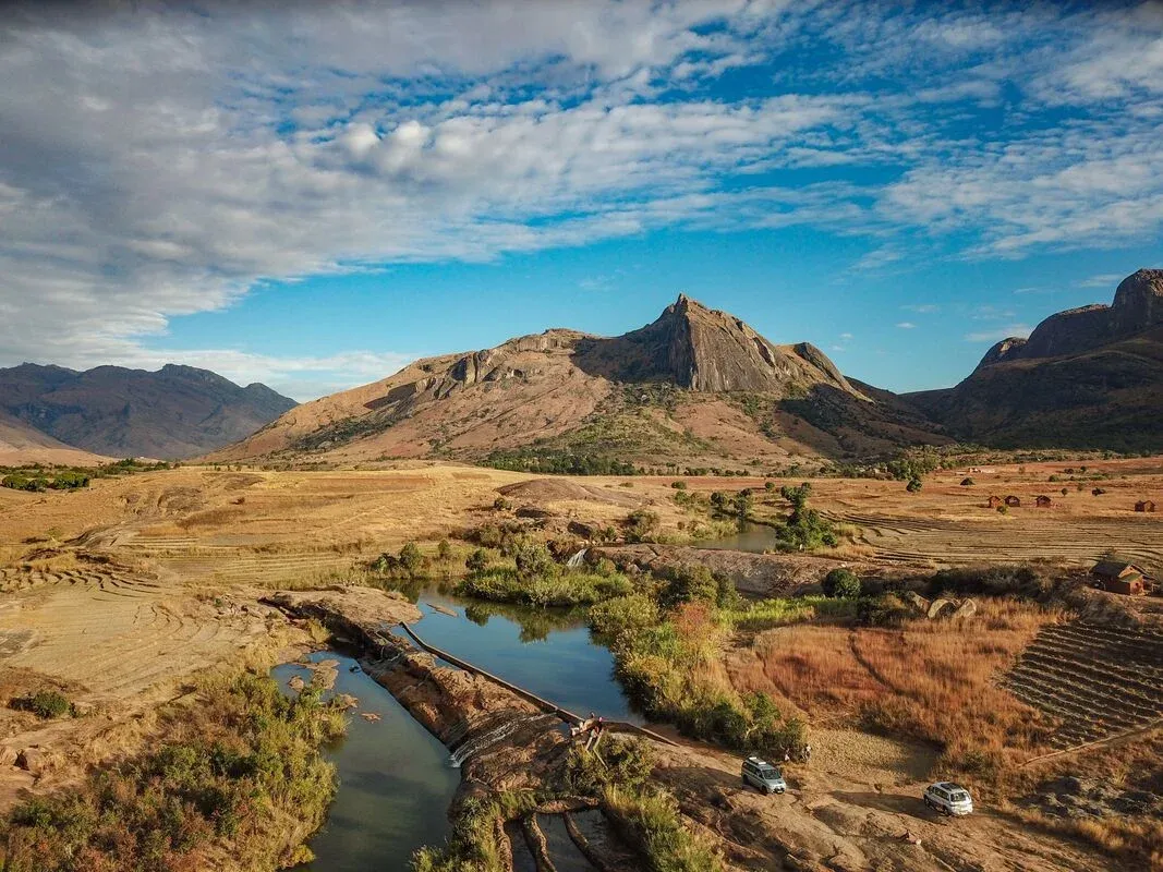 Paysage aride de Madagascar avec montagnes rocheuses et rivière traversant des terres agricoles sous un ciel dégagé
