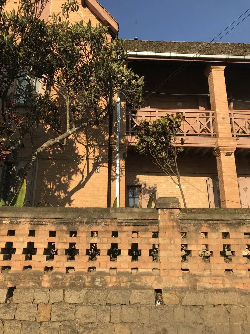 Maison en pierre avec balcon en bois et mur en briques ornées à Madagascar sous un arbre