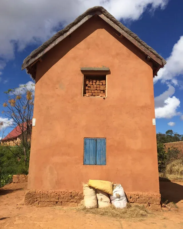 Maison en terre cuite aux murs ocres avec sacs au sol et petit fenêtre bleue dans région rurale