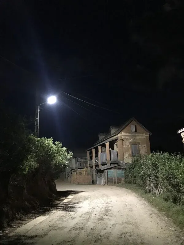 Chemin rural nocturne éclairé menant à une vieille maison en pierre entourée de végétation