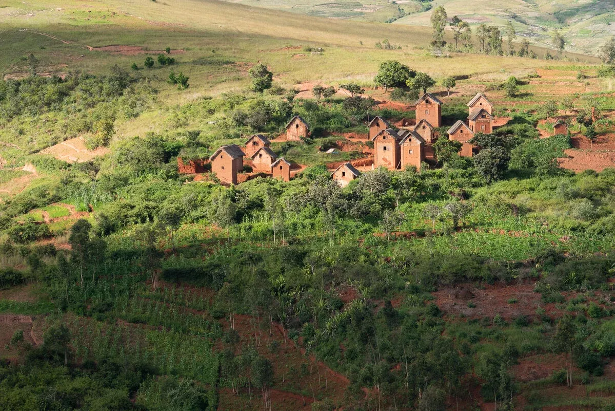 Village traditionnel en terre rouge niché dans un paysage verdoyant et vallonné de Madagascar